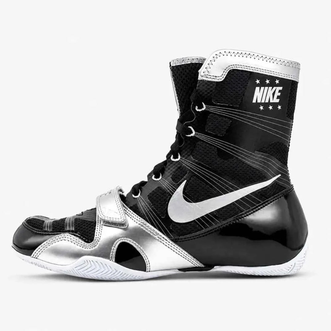 A Nike high-top boxing shoe in black and metallic silver, featuring a prominent silver swoosh and white Nike branding on the ankle collar, shown against a light gray background.