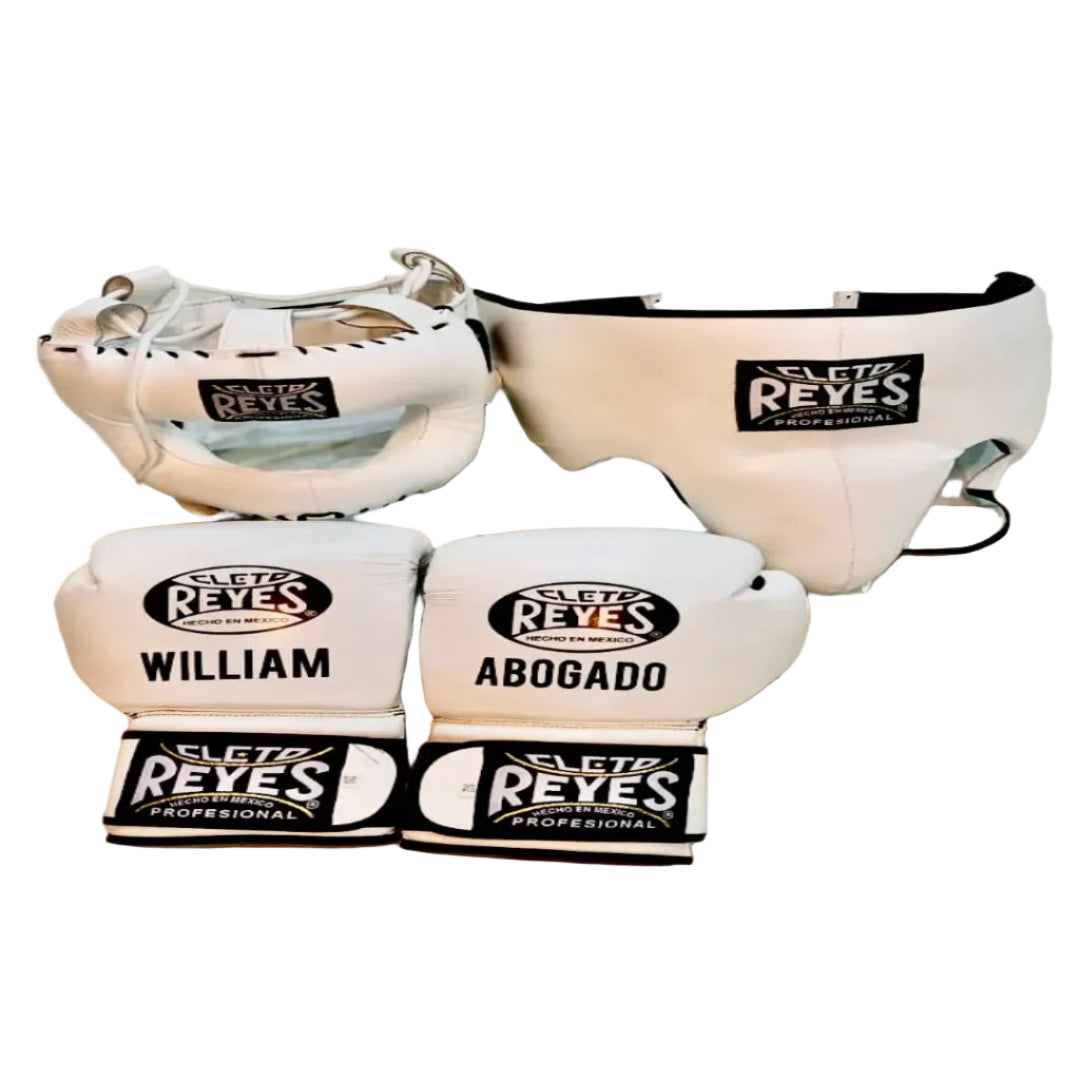 A set of white Sleta Reyes boxing gear, including a headguard, chest protector, and boxing gloves, laid out on a light beige tiled floor. Two of the gloves are personalized with the names 'WILLIAM' and 'ABOGADO'.