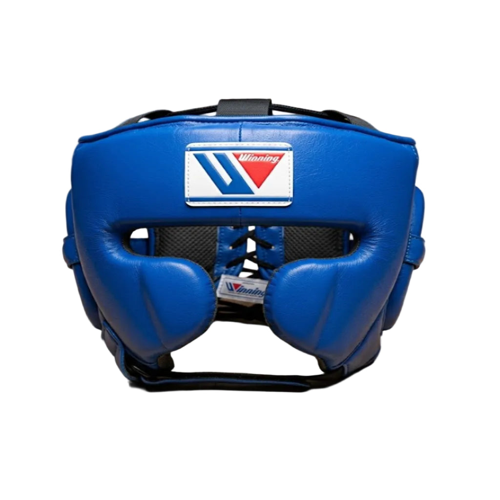 A blue Muay Thai headgear with a visible Venum logo patch on the forehead, resting on a light wood floor with a brick wall in the background.