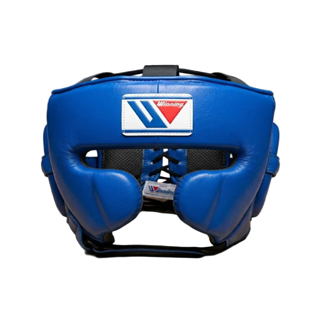 A blue Muay Thai headgear with a visible Venum logo patch on the forehead, resting on a light wood floor with a brick wall in the background.