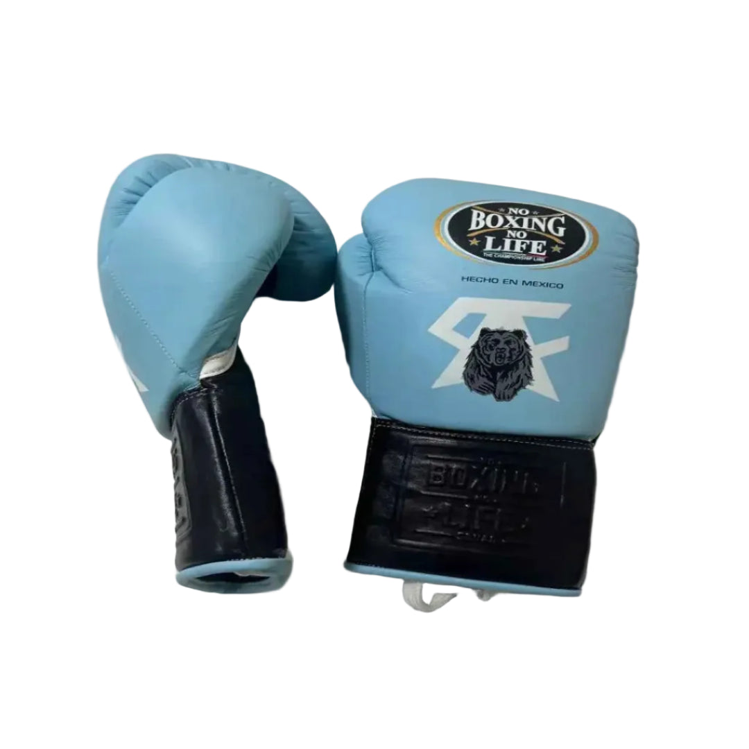 A pair of boxing gloves in light blue and black, with one glove showing the front with a 'Boxing for Life' logo and a bear graphic, and the other showing the padded black wrist strap. They are placed on a crumpled white sheet.