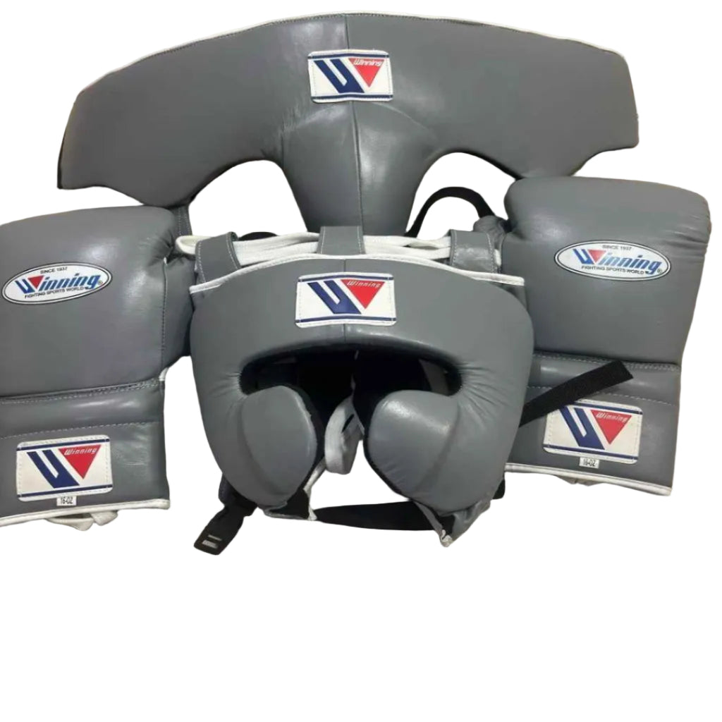 Gray boxing headgear and gloves with a brand logo on a beige surface