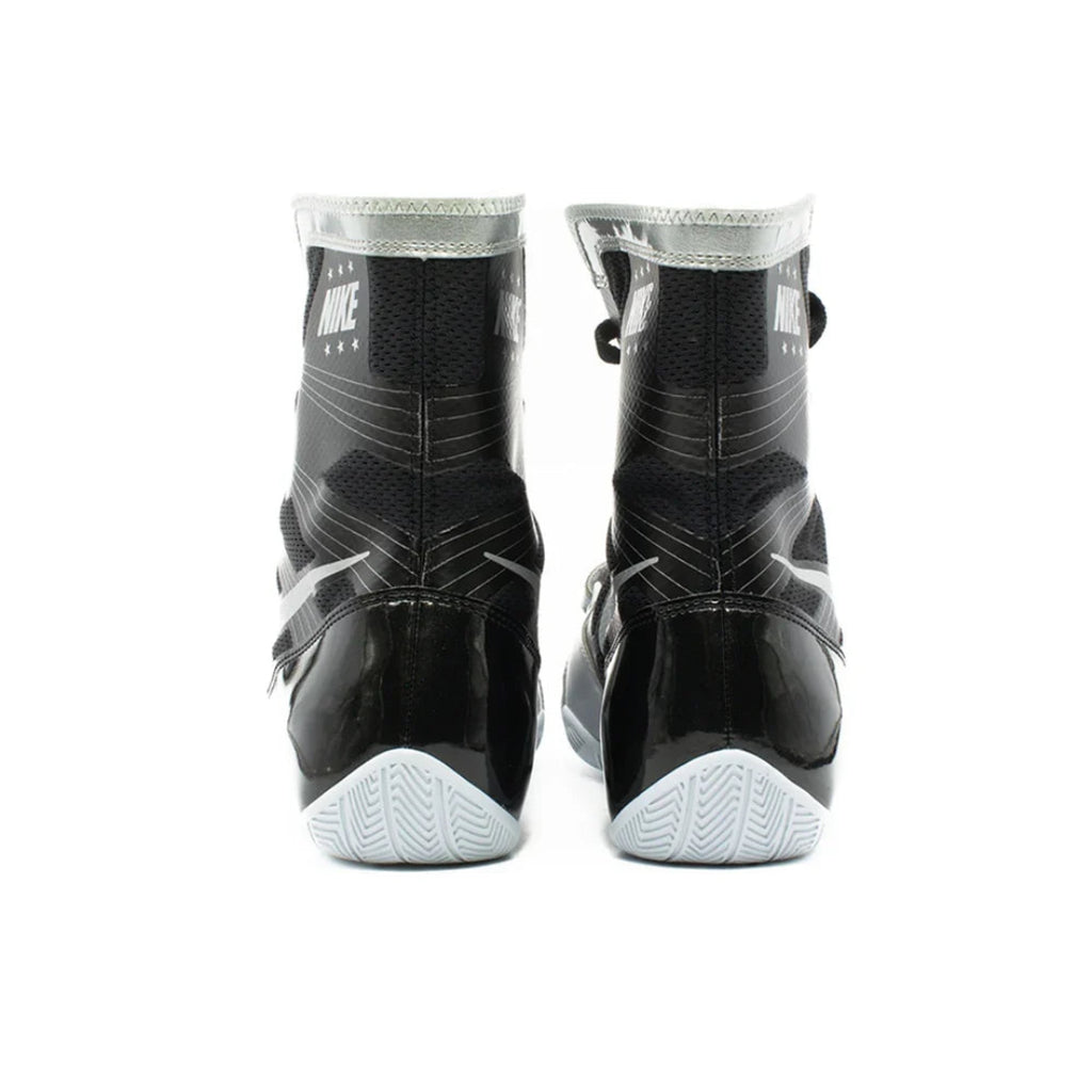 A pair of Nike high-top athletic boots shown from the back, featuring a black and gray textured upper with glossy black patent panels and light gray soles.